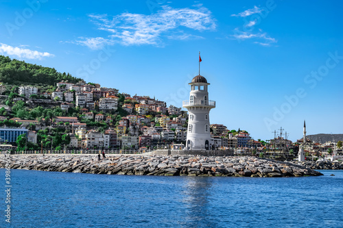 Alanya, Turkey - October 22, 2020: Panorama of Alanya with a white old lighthouse on the background of modern cottages on a mountainside. Beautiful cityscape and seascape in summer-autumn sunny day