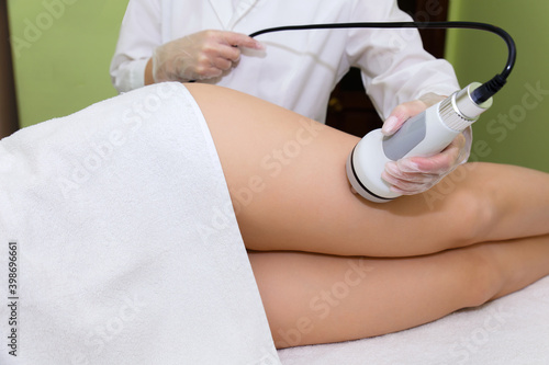 The beautician holds the handpiece in his hand and guides the client along the thigh and buttocks. RF lifting procedure in the spa salon.