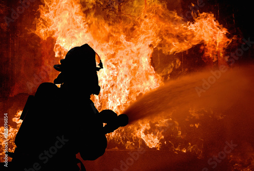 Fototapeta Silhouette of Firemen fighting a raging fire with flames