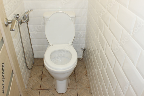 White toilet bowl in a white room. Washroom white with beige tiles on the floor