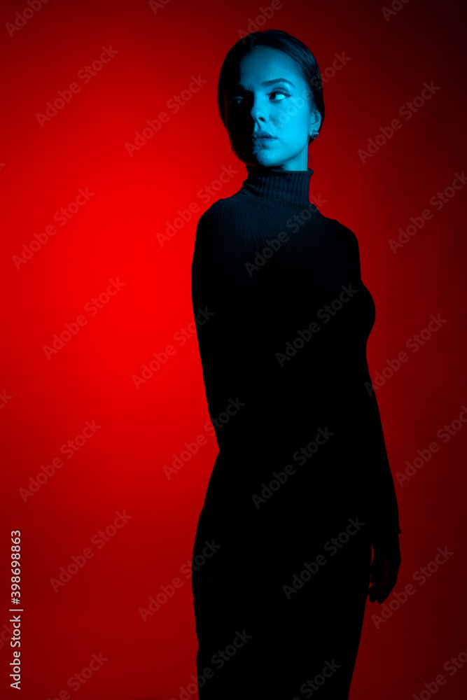 Portrait of young woman in the studio with red and blue lights wearing all black outfit facing the other way