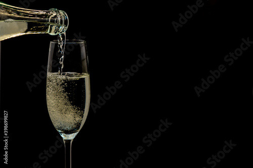 Pouring gold champagne into glass, a lot of bubbles insidde, isolated on black background, white froth on the top