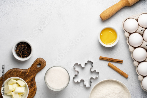 Flat lay with baking ingredients for gingerbread. Wheat flour, sugar, rolling pin, butter, honey, cinnamon sticks, cloves, cookie cutter and white eggs on grey background. Top view, copy space. 