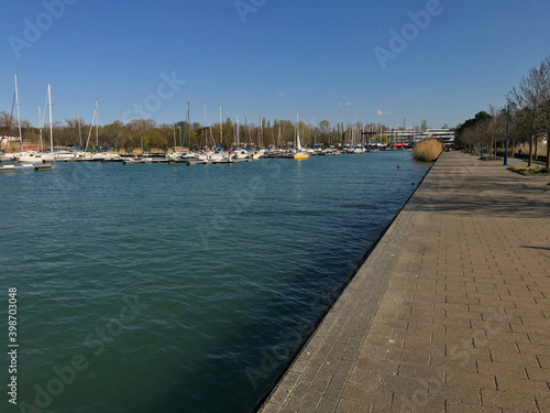 Empty, straight port coastline with a pier and a small port with sailing ships and boats, blue water and sky, turquoise water, summer, sunny day. 