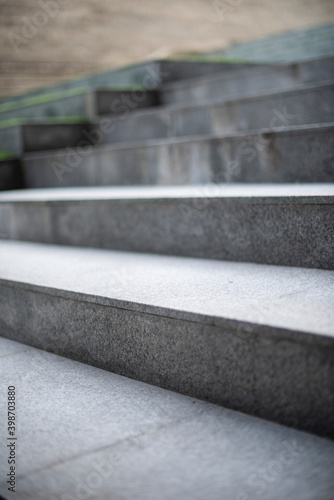 Neat and tidy grey stair steps made of stone and granite tiles with a curb, side by side with green steps in a modern hotel leading to a lobby area, close up.