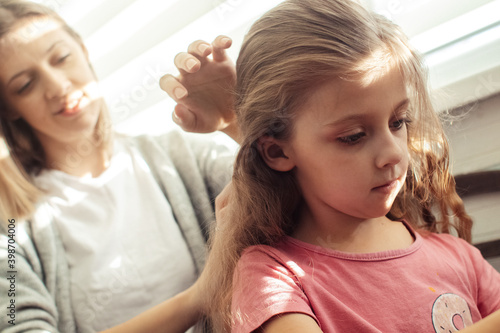 Mom is combing her daughter's hair. Taking care of baby's hair. The concept of a happy childhood and a good attitude towards children. Happy family