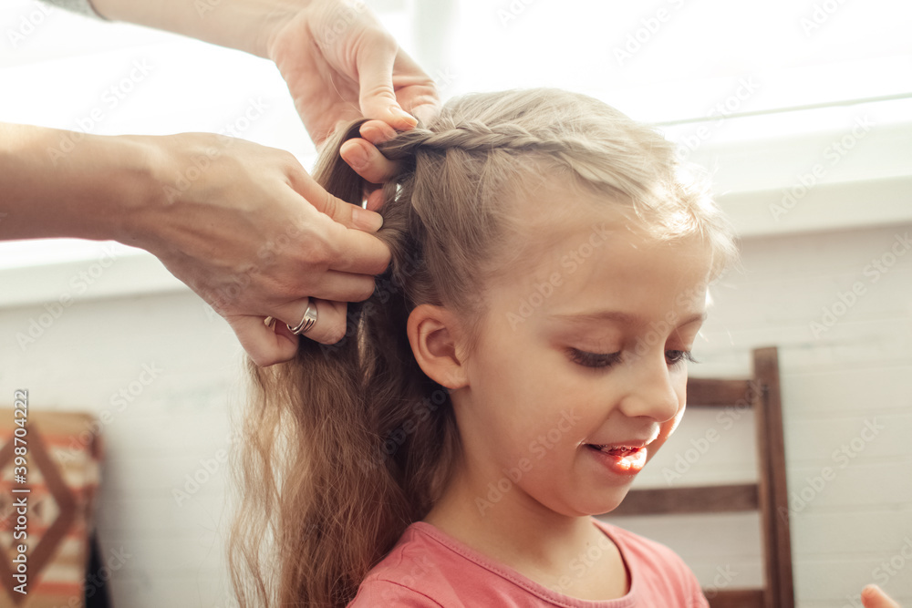 Fototapeta premium Mom is combing her daughter's hair. Taking care of baby's hair. The concept of a happy childhood and a good attitude towards children. Happy family
