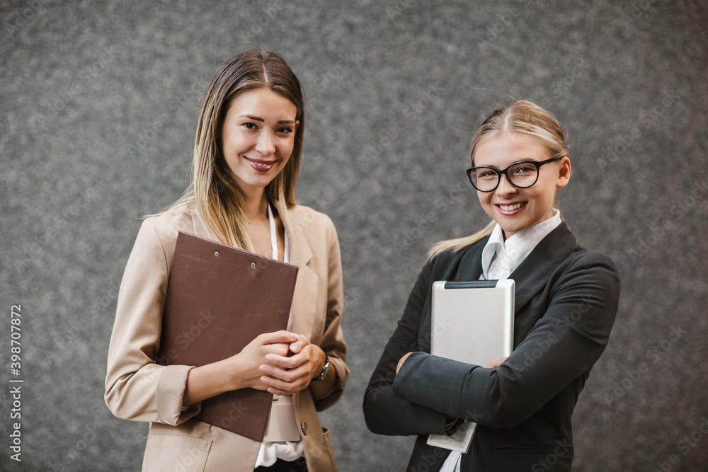 Portrait of two successful businesswomen holding digital tablet and clipboard