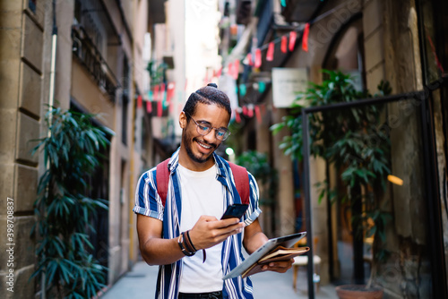 Smiling ethnic guy messaging on smartphone on street