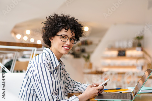 Beautiful happy woman using cellphone while working with laptop