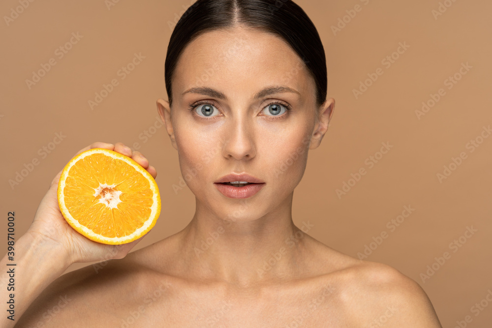 Woman with perfect face skin, combed hair, squeezing orange. Confident female with natural makeup and citrus fruit on studio beige background. Vitamin C, slimming diet, antioxidant concept. Woman with perfect face skin, combed hair, squeezing orange. Confident female with natural makeup and citrus fruit on studio beige background. Vitamin C, slimming diet, antioxidant concept.