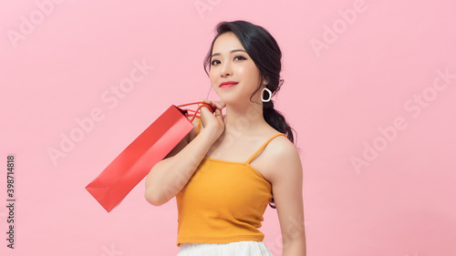 Portrait of a smiling young girl holding shopping bags and looking away at copy space isolated over pink background