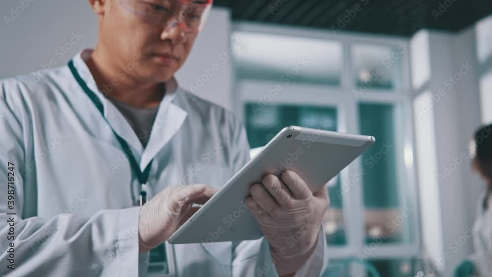 Close-up of japanese professional expert working in medical laboratory performing research with digital pc tablet computer. Lab engineer. Scientist at work. Close-up of japanese professional expert working in medical laboratory performing research with digital pc tablet computer. Lab engineer. Scientist at work.