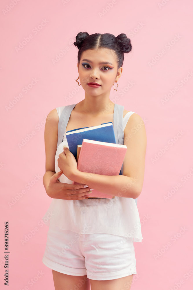 Photo of pretty student girl 20s with double buns hairstyle wearing backpack holding many studying books isolated over pink background Photo of pretty student girl 20s with double buns hairstyle wearing backpack holding many studying books isolated over pink background