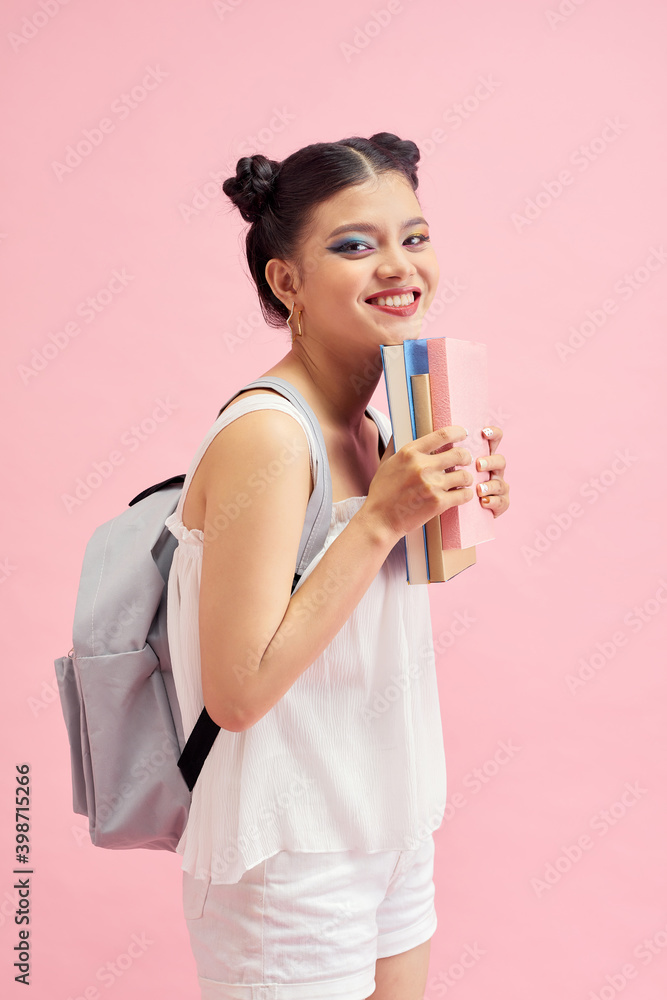 Young reader girl lifts her palm up holding colored books and smiling isolated on vivid pink background Young reader girl lifts her palm up holding colored books and smiling isolated on vivid pink background