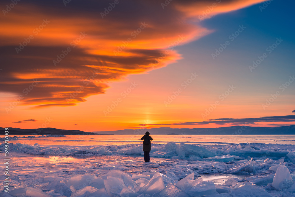 Traveler take photo sunset on natural breaking ice in frozen water at Lake Baikal, Siberia, Russia.