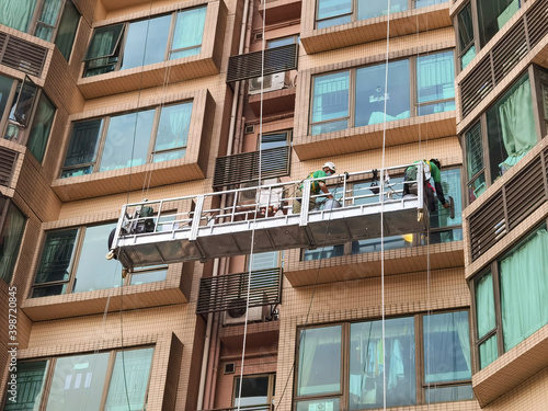 Two Professional workers use a suspended cradle or steeplejack to access and clean windows of typical high rise building or skyscraper in Hong Kong before Christmas or New Year.
