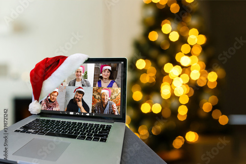 Computer in cozy room with hanging red hat and with Santa Claus on screen wishing Merry Christmas and Happy New Year online photo