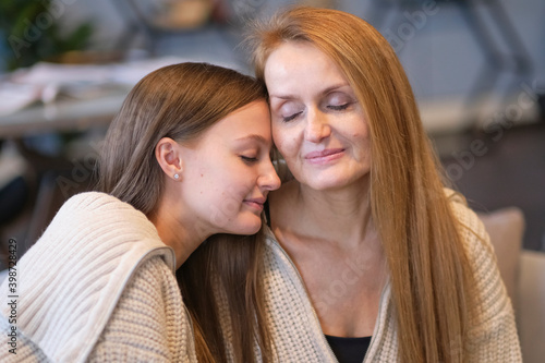 Cheerful young woman hugging aged mother sitting on sofa while resting together in living room at home. joyful mam and friendly daughter holding hands looking at each other.