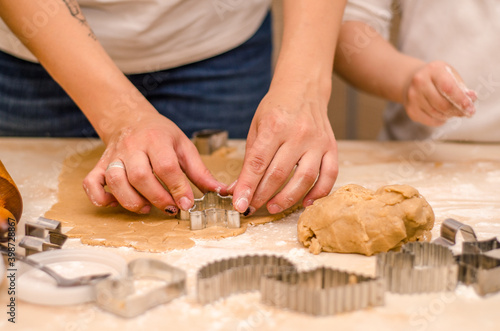 Hands of mother and daughter prepare gingerbread cookies for christmas, they roll out dough and cut cookies