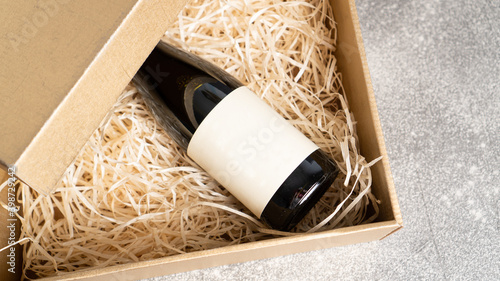 Present box with a bottle of wine with a blank label. Birthday present. Wine bottle in a wooden box with hay
