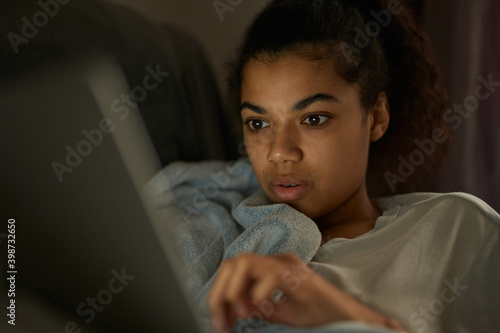 Study at home. Close up portrait of mixed race girl in casual wear working with laptop  lying on the sofa at home during coronavirus lockdown. Online education  work from home concept