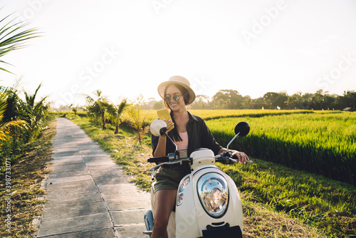 Cheerful female tourist enjoying smartphone messaging with network followers during travel vacations in Vietnam, happy hipster girl using mobile app for tracking location gps during scooter driving