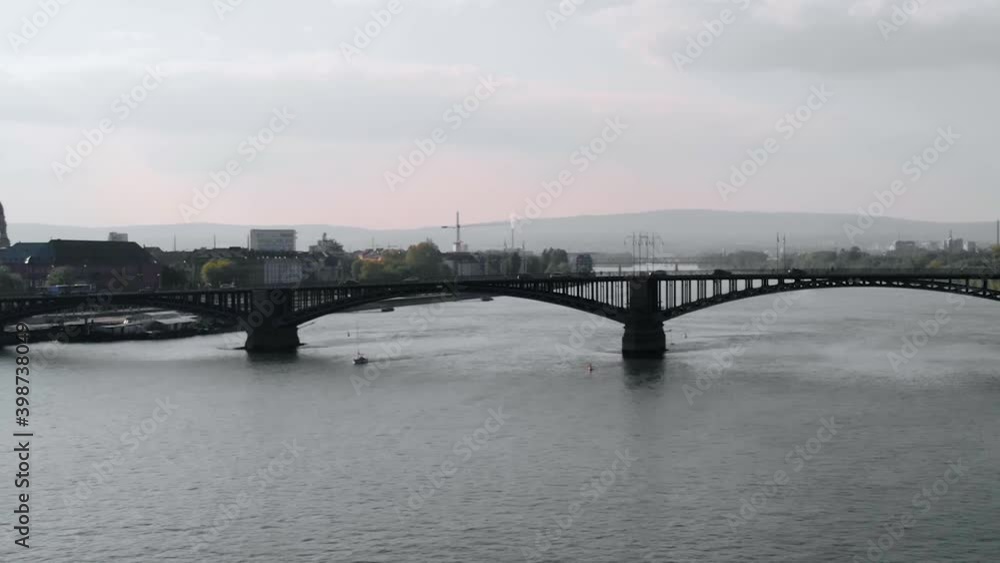 Aerial view of a sailboat moving under a bridge, on Rhein river, cloudy day, in Mainz, Germany - pan, drone shot Aerial view of a sailboat moving under a bridge, on Rhein river, cloudy day, in Mainz, Germany - pan, drone shot