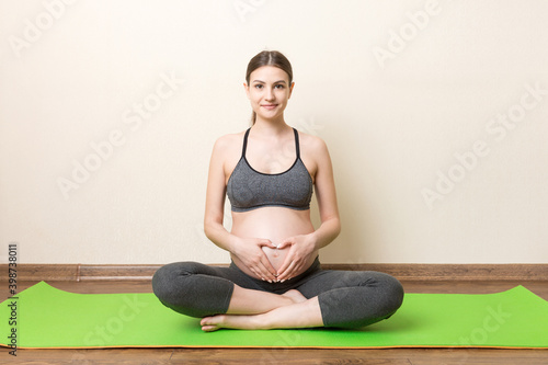Fototapeta Naklejka Na Ścianę i Meble -  Pregnant woman exercising on orange mat in room. Pregnancy Yoga and Fitness concept at coronavirus time