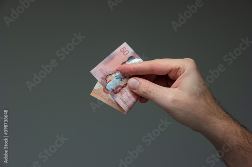Caucasian male hand holding a folded 50 Canadian dollar bill close up shot isolated on gray photo