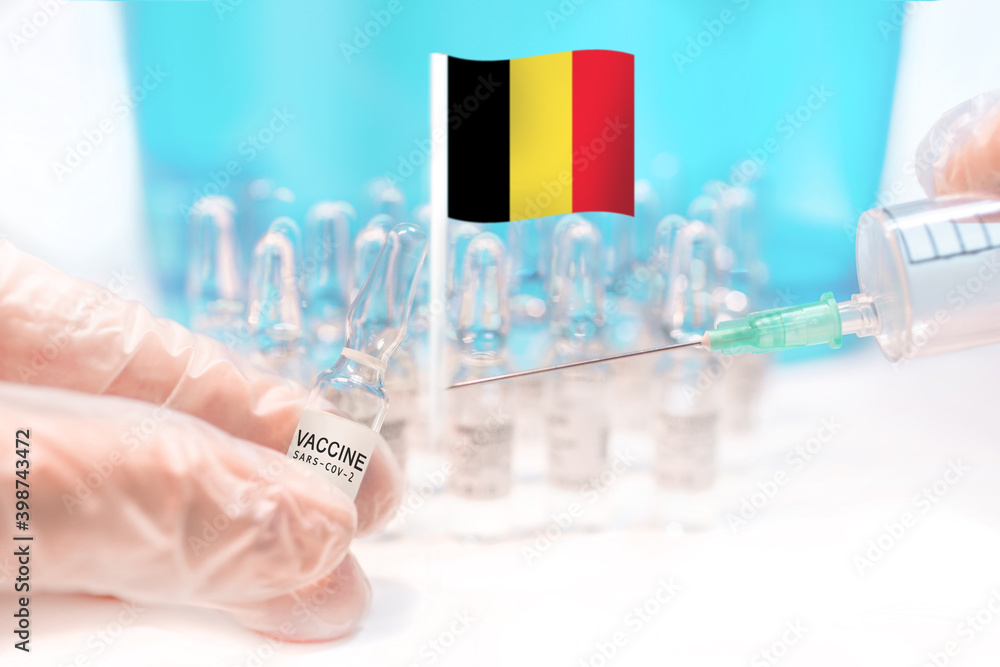 Hands holding a vaccine vial and a syringe with rows of the same capsules and a flag of Belgium in the background, illustrating plans for global vaccination against Covid-19 (SARS-CoV-2, coronavirus). Hands holding a vaccine vial and a syringe with rows of the same capsules and a flag of Belgium in the background, illustrating plans for global vaccination against Covid-19 (SARS-CoV-2, coronavirus).
