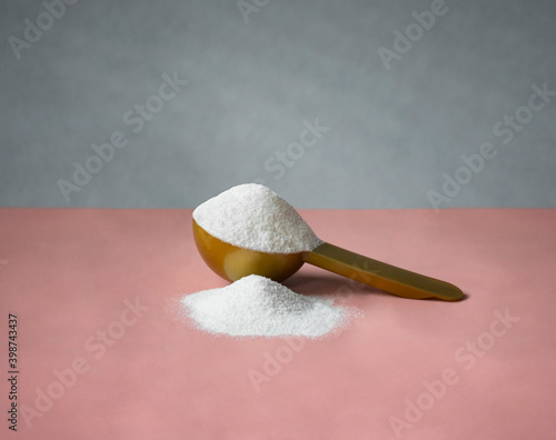 Gold measuring spoon with collagen on pastel pink gray background. Powdered hydrolyzed fish collagen supplement.