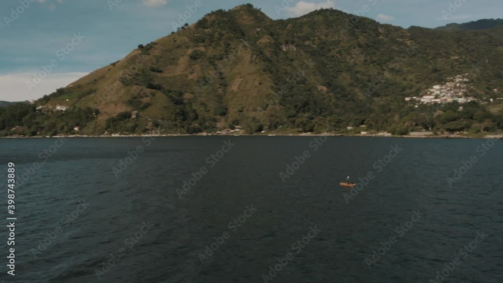 Drone aerial view of lake Atitlan, a man paddling on a boat and the beautiful volcanoes of Guatemala