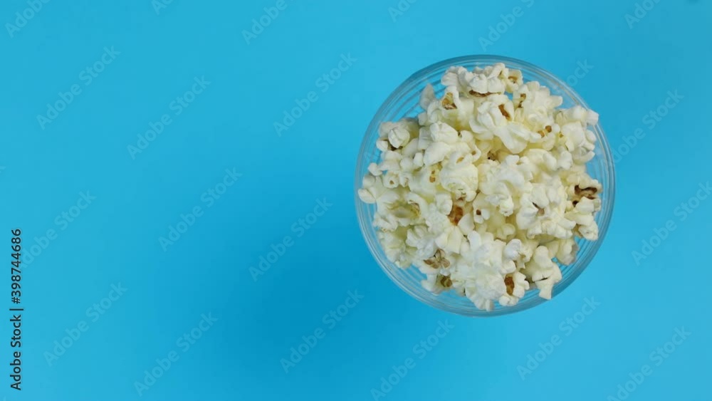 Popcorn in a plate on one edge of the frame, rotating on a blue background. Space for text. Popcorn in a plate on one edge of the frame, rotating on a blue background. Space for text.