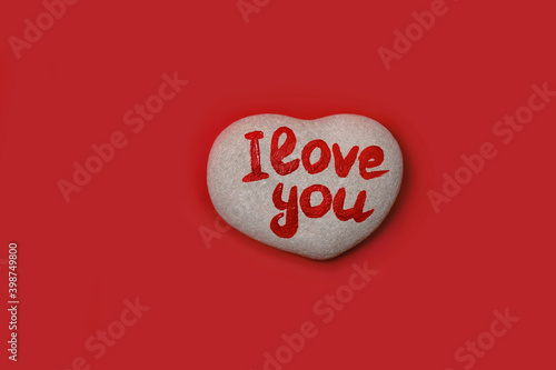 stone in shape of heart with inscription written by hand I love you on red background