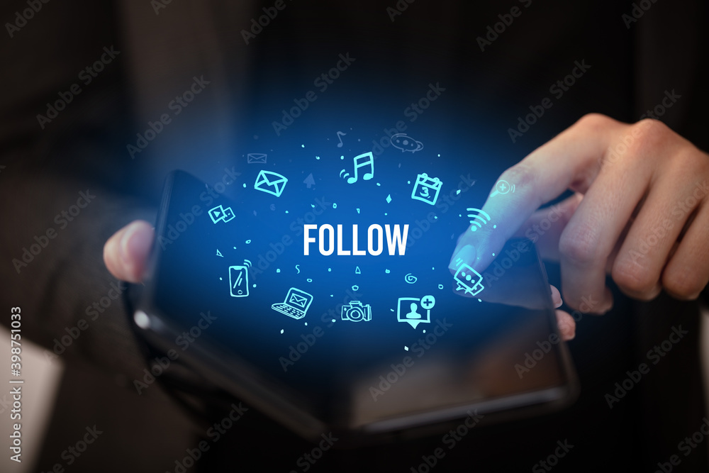 Businessman holding a foldable smartphone with FOLLOW inscription, social media concept Businessman holding a foldable smartphone with FOLLOW inscription, social media concept