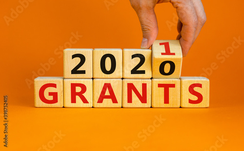 Symbol of 2021 New Year. Male hand flips wooden cubes and changes the inscription 'Grants 2020' to 'Grants 2021'. Beautiful orange background, copy space. Business and 2021 new year grants concept.