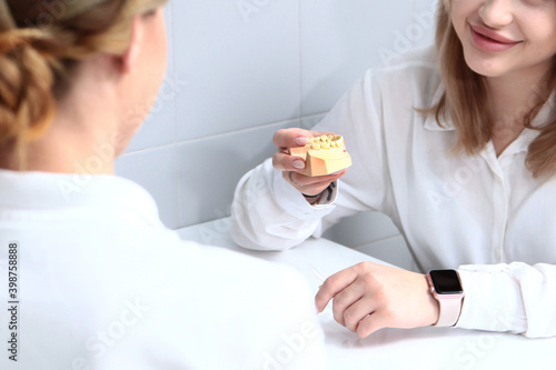 The patient is talking to the dentist. The girl holds a cast of teeth in her hand. Unrecognizable people. Photo on a light background.