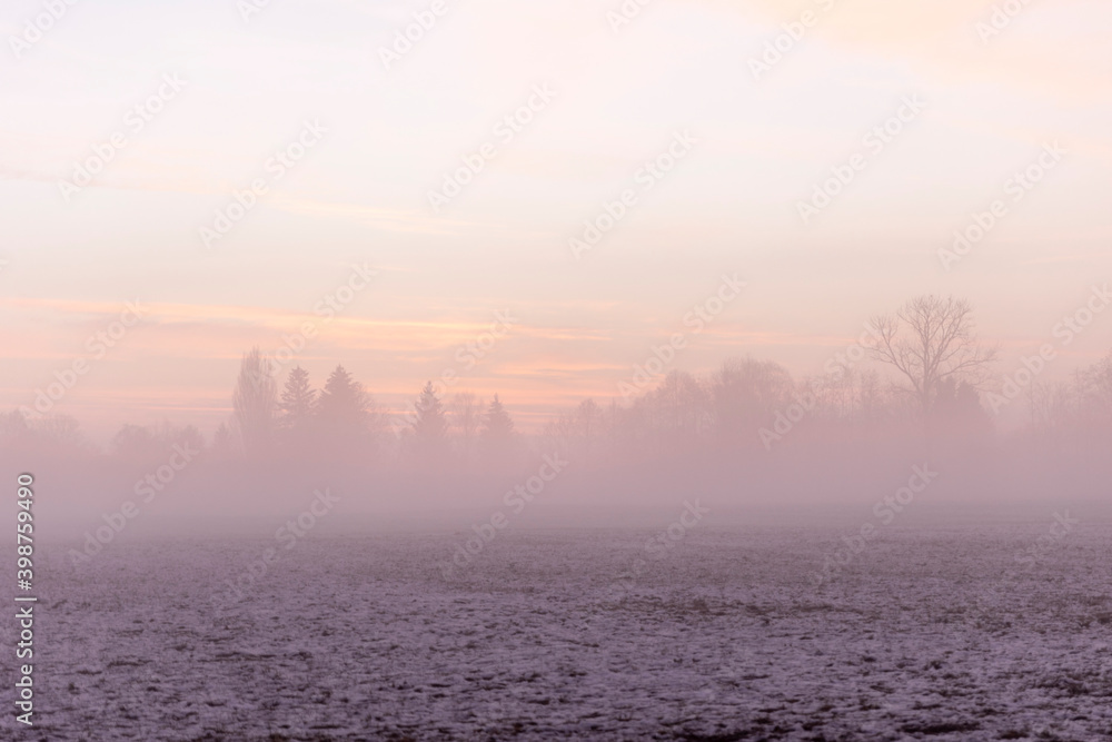 Sunrise over snow covered meadow with ground fog in winter