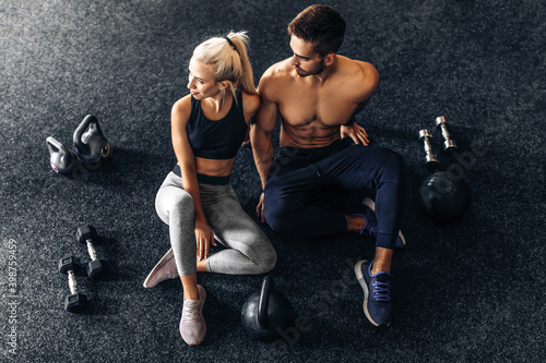 Young couple of athletic people sitting together on the floor of the gym, with dumbbells, together after training in the gym
