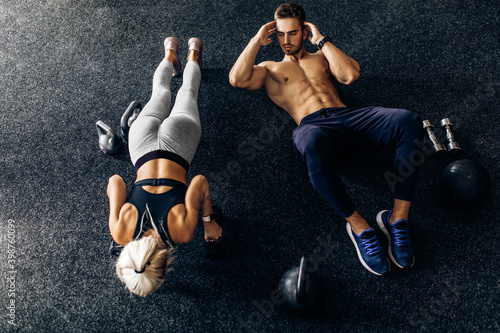 young couple, man and woman doing abdominal exercises with dumbbells, on the floor in the gym