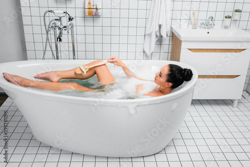 фотографія woman using brush in bathtub with lather in modern bathroom
