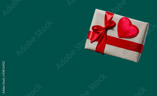 Decorated gift box with red heart and ribbon on the green background as a concept of holiday gifts and congratulations
