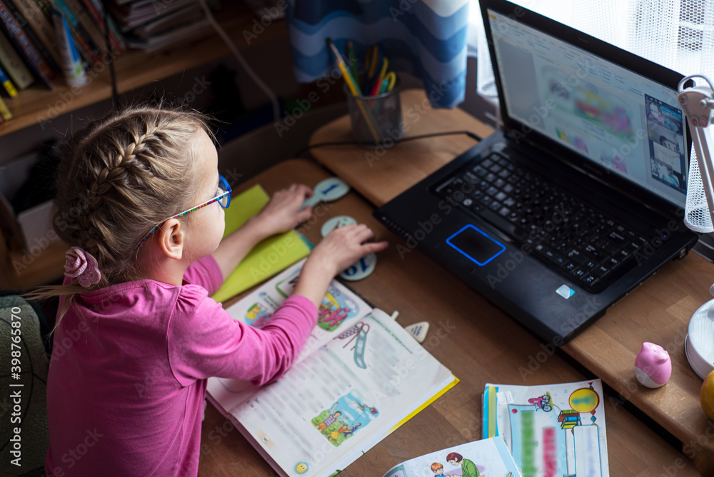 Little girl in eyelgasses studying online and using her laptop at home Little girl in eyelgasses studying online and using her laptop at home