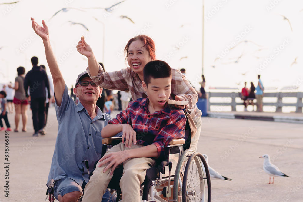 Asian Disabled child on wheelchair and parents the outdoors nature and seagull birds background,Boy frightened expression afraid of the bird, Happy disability kid travel in family holiday concept. Asian Disabled child on wheelchair and parents the outdoors nature and seagull birds background,Boy frightened expression afraid of the bird, Happy disability kid travel in family holiday concept.