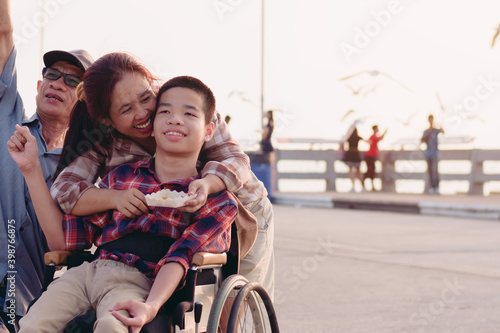 Asian Disabled child on wheelchair and parents the outdoors ​nature​ and seagull birds background​,Life in the education age of special children,Happy disability kid travel in family holiday concept. © GAYSORN