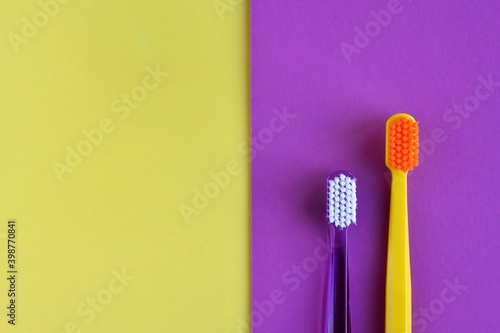 two plastic purple and yellow toothbrushes on color block paper background. Health care concept. Man and woman teeth hygiene. Living together. 