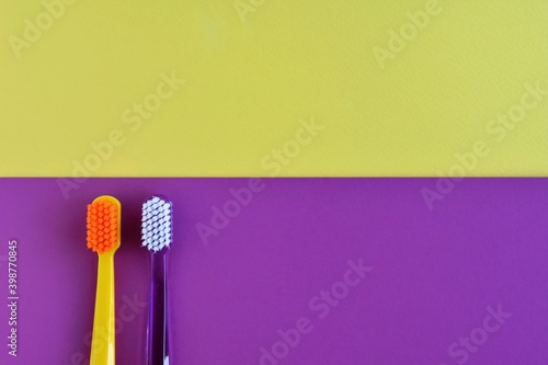 two plastic purple and yellow toothbrushes on color block paper background. Health care concept. Man and woman teeth hygiene. Living together.  © Tetiana Ivanova
