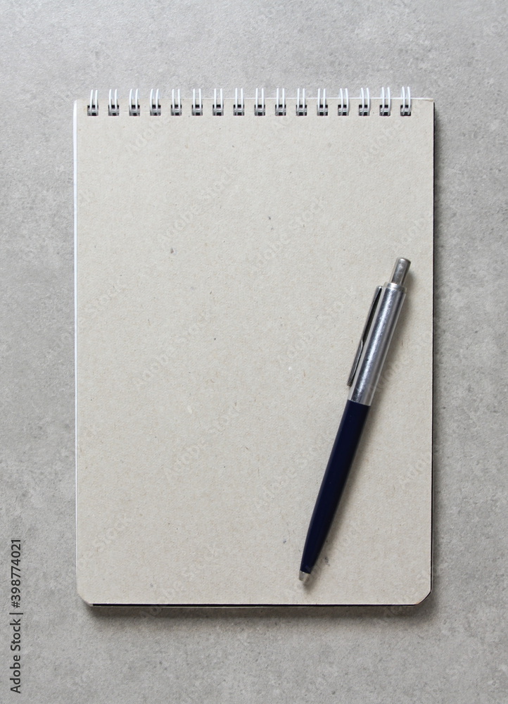A spring notebook with a sheet of craft paper A5 with a ballpoint pen on light grey concrete background. Concept of new idea, business plan and strategy. Empty space for text A spring notebook with a sheet of craft paper A5 with a ballpoint pen on light grey concrete background. Concept of new idea, business plan and strategy. Empty space for text