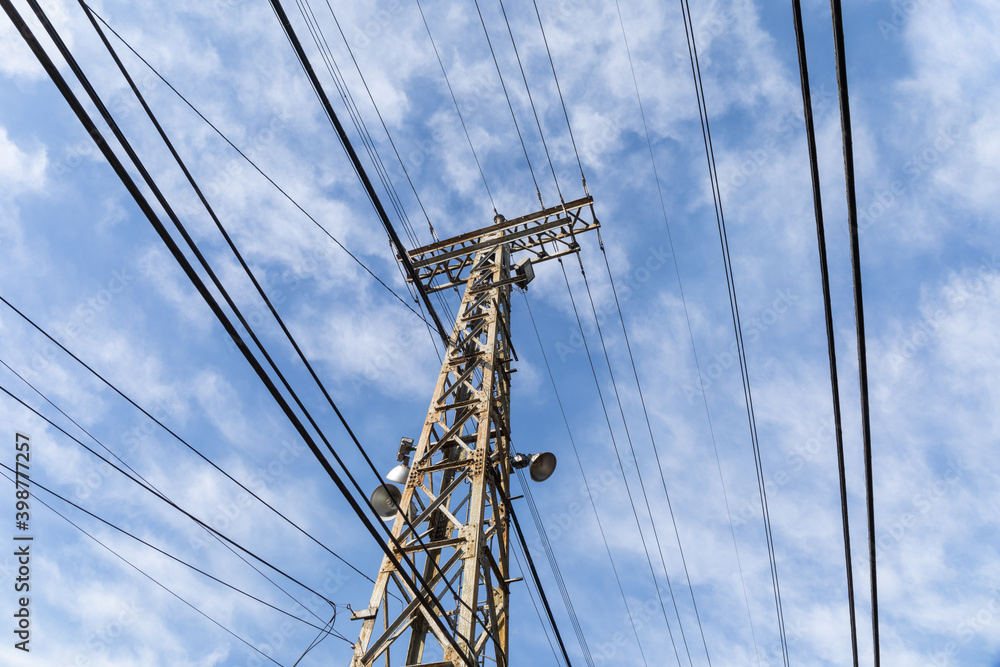 Extreme upward view of an old metal electrical tower with cables attached and alongside against a blue sky with clouds, horizontal aspect